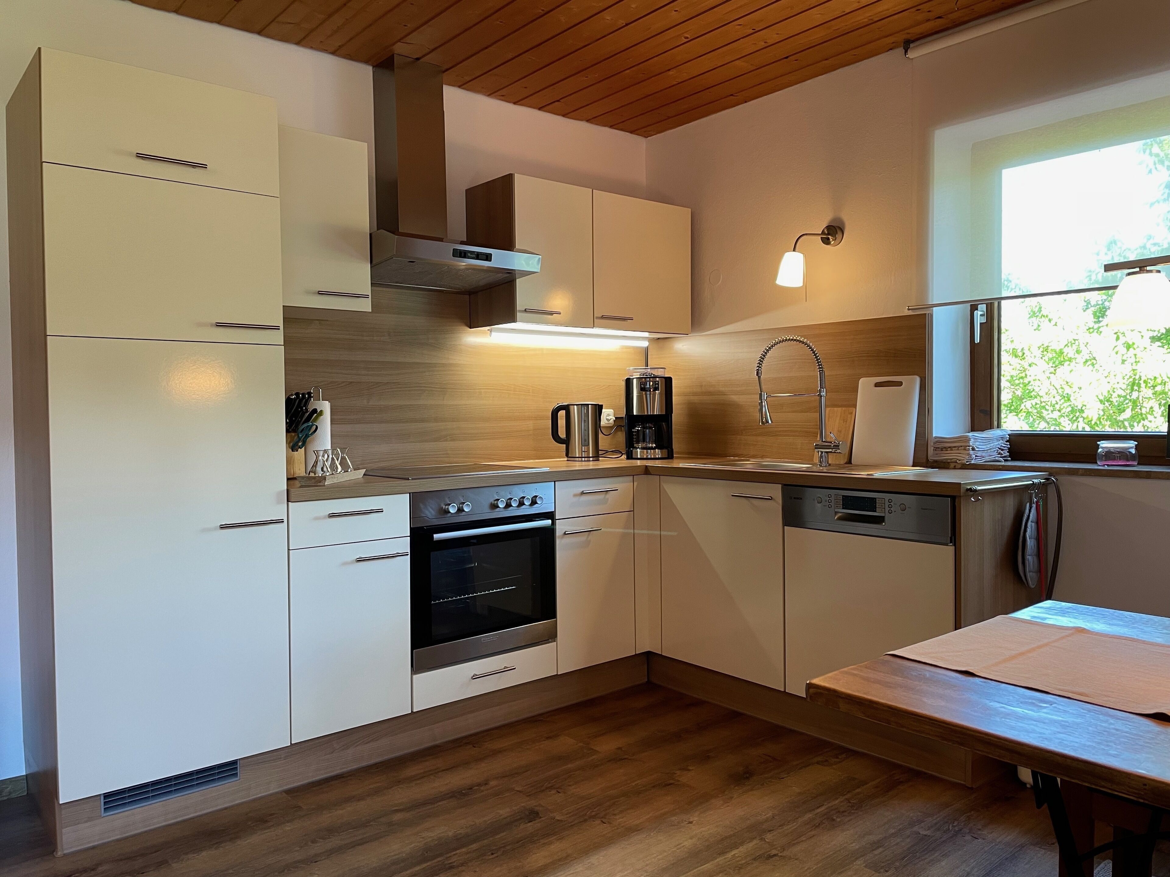 Eine moderne Küche mit Holzausstattung, Backofen, Kaffeemaschine und einem Fenster mit Blick auf Grünflächen.