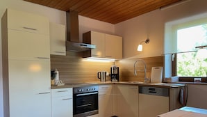 A modern kitchen with wooden cabinets, a built-in oven, a coffee maker, and a window with a view of greenery.