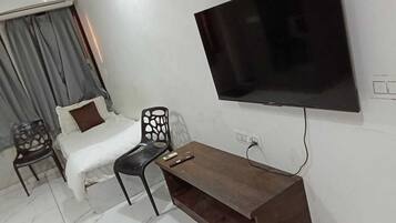 A hotel room with a bed, two chairs, a wooden table, and a TV mounted on the wall.
