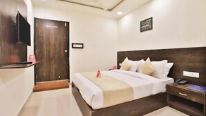 Una habitación de hotel con cama, mesita de noche y televisor montado en la pared.