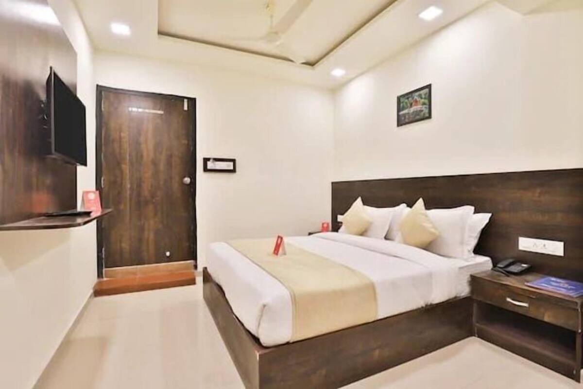 Una habitación de hotel con cama, mesita de noche y televisor montado en la pared.