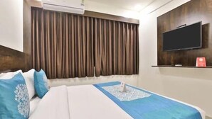 Habitación de hotel con cama, televisor de pantalla plana en la pared y ventana con cortinas.