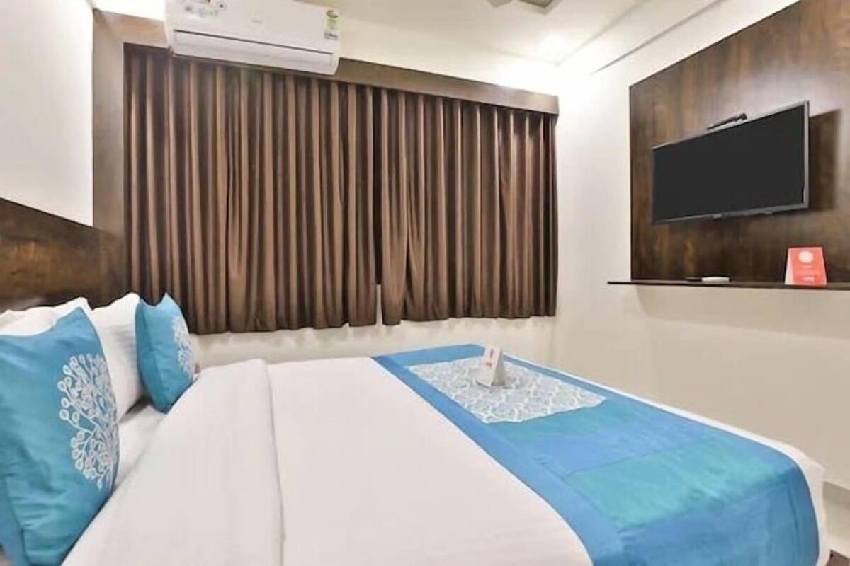 Habitación de hotel con cama, televisor de pantalla plana en la pared y ventana con cortinas.