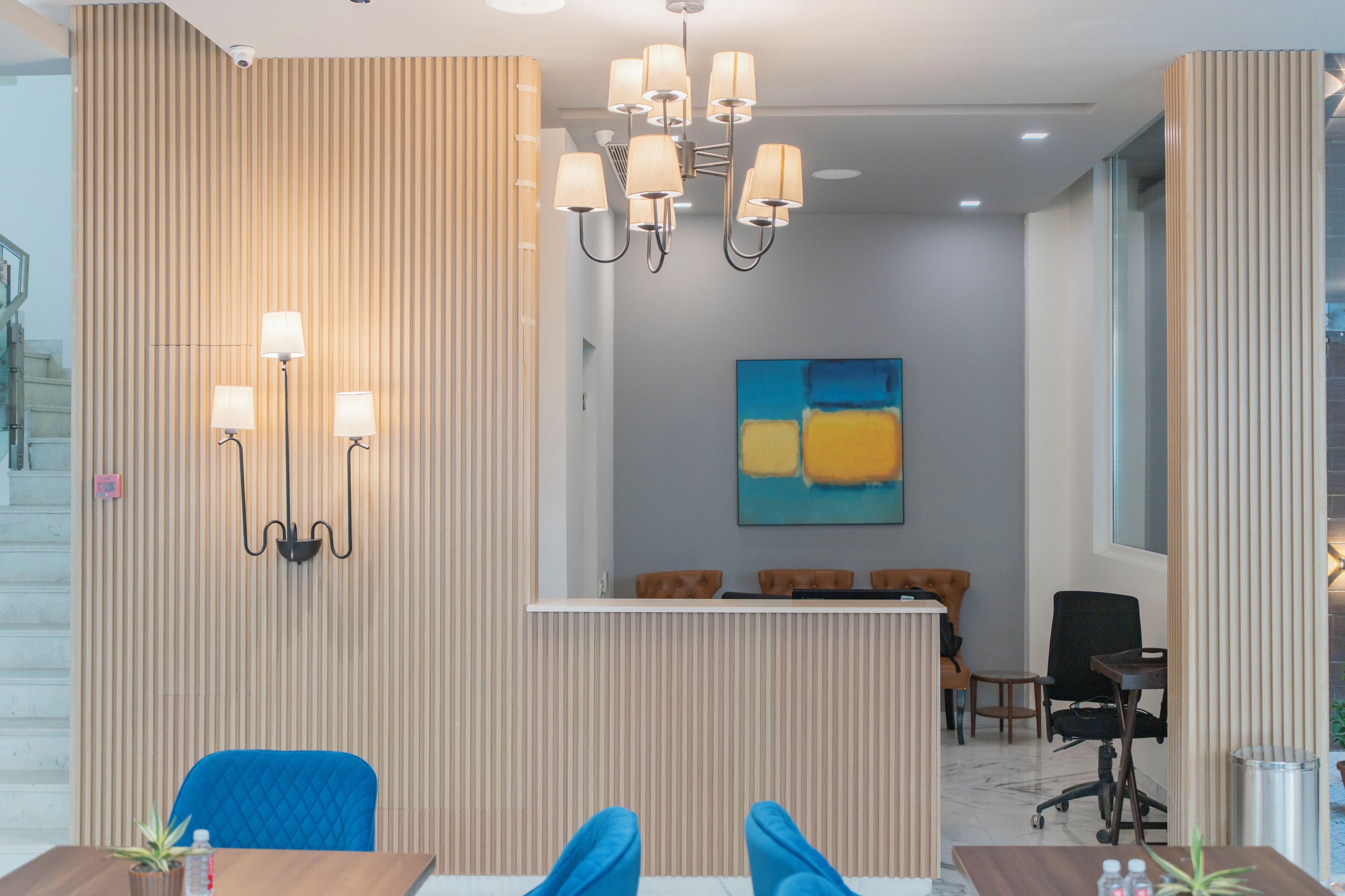 A modern reception area with a wooden panel wall, a chandelier, a reception desk, and a blue chair.