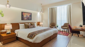 Habitación de hotel con una cama grande, un escritorio, dos sillas, un ventilador de techo y una ventana con cortinas.
