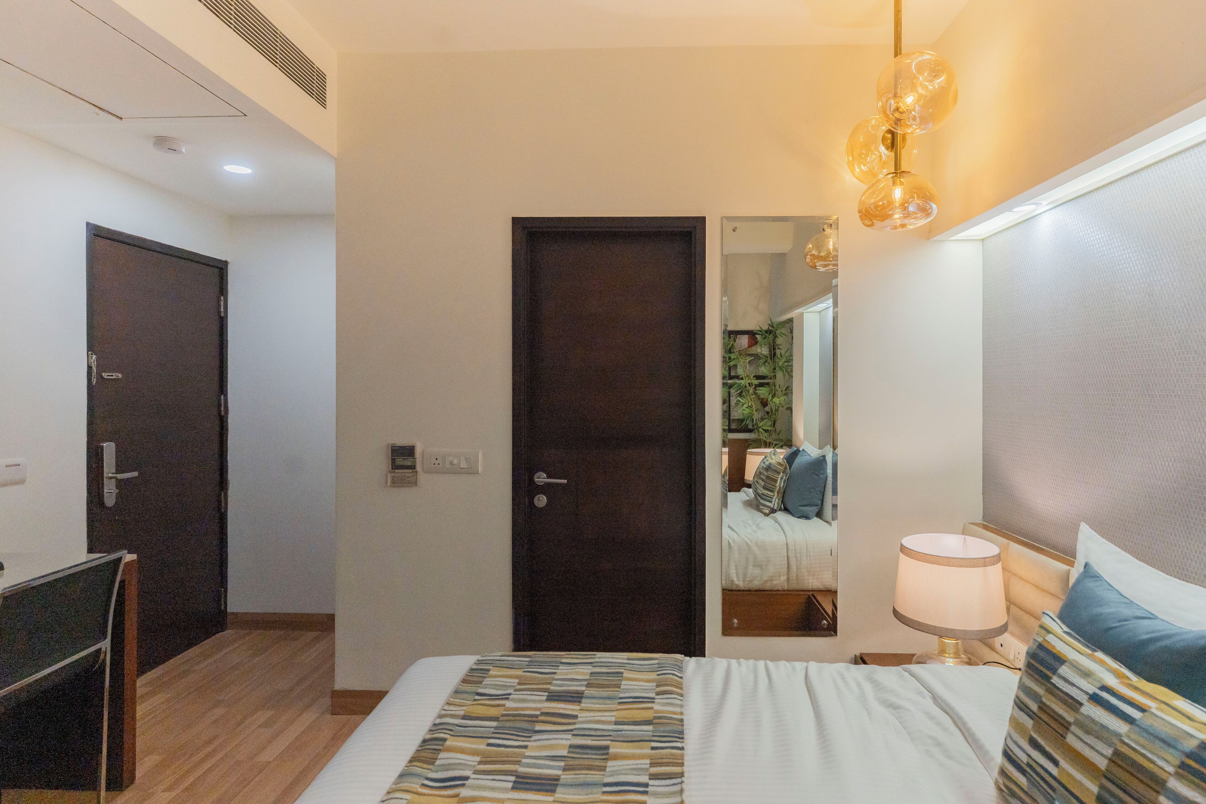 A hotel room with a bed, bedside table, lamp, and a door leading to another room.