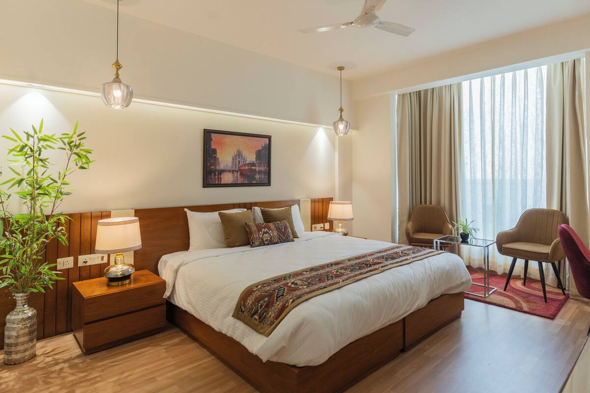 A hotel room with a large bed, bedside lamps, a nightstand, a chair, a table, and a window with curtains.