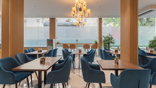 Un comedor moderno con sillas tapizadas en azul, mesas de madera y una lámpara central.