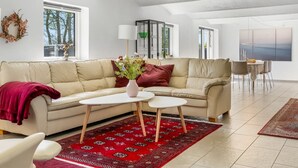 Un salon spacieux avec un canapé beige, un tapis à motifs rouges et une table basse blanche.