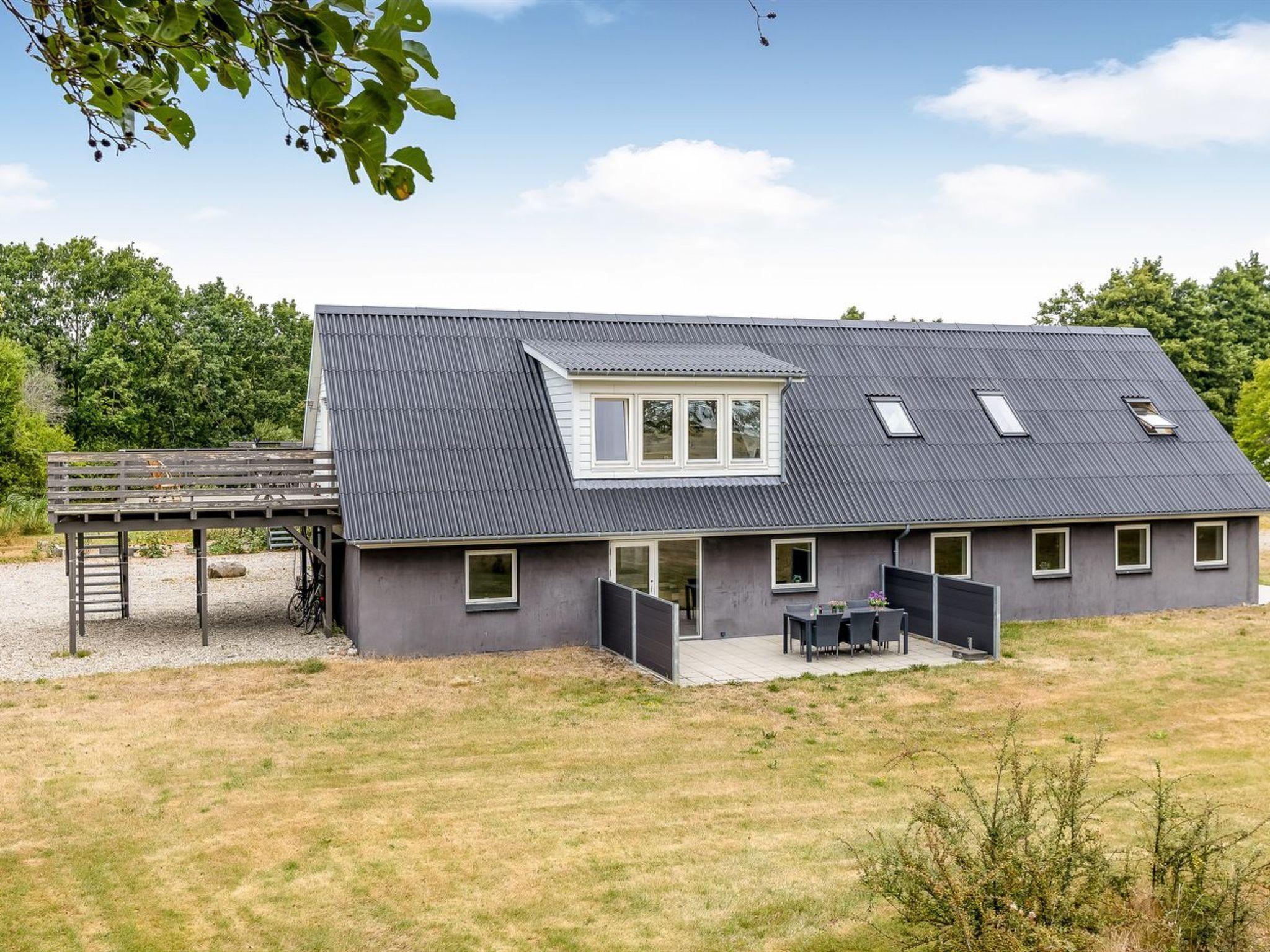 Ein modernes Haus mit Satteldach, überdachter Terrasse und umzäunter Gartenfläche.