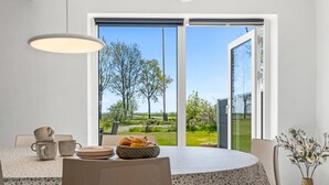 Un coin repas comprenant une table, des chaises et donnant sur un paysage verdoyant grâce à une porte vitrée.