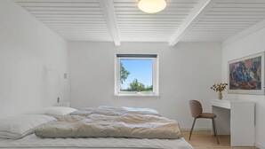 Une chambre à coucher avec un lit, un bureau, une chaise, une fenêtre et un tableau accroché au mur.