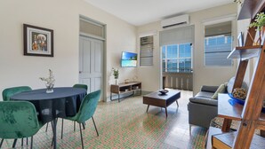 A living room with a dining area, a TV mounted on the wall, and a view through the window. - Apartment in Miramar for 6 People with a Power Generator (San Juan)