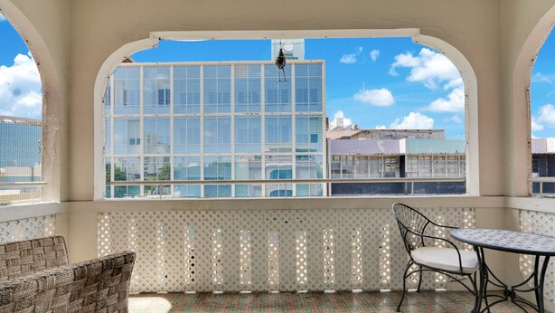 A balcony with a view of a building, a lattice screen, a wicker chair, and a metal table. - Apartment in Miramar for 6 People with a Power Generator (San Juan)