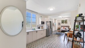 Una cocina moderna con un espejo grande, un área de comedor con una mesa y sillas de madera, y una sala de estar con un sofá y una televisión.