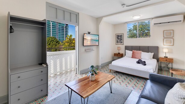 Un dormitorio moderno con cama, mesitas de noche, armario, una pequeña mesa con una planta y vistas al exterior.