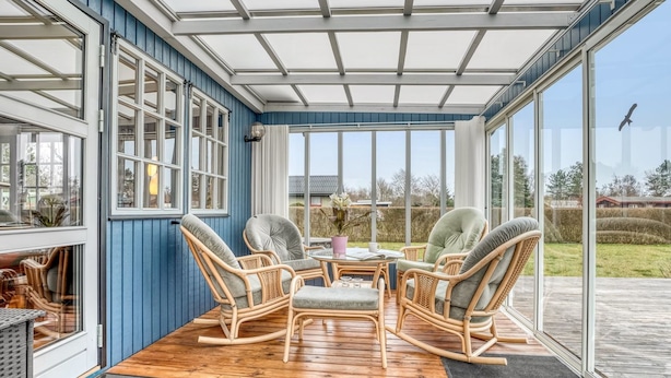 Een veranda met rieten stoelen, een tafel en uitzicht op de omgeving.