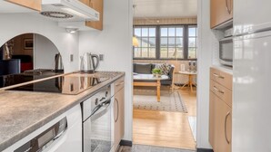 Een moderne keuken met een ingebouwde oven, waterkoker en magnetron. Door een open deur is een eethoek met tafel en stoelen zichtbaar.