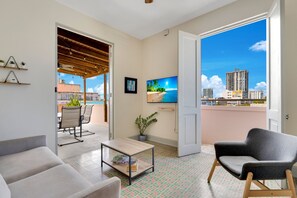 A modern living room with a sofa, a coffee table, and a chair. There is a TV mounted on the wall and a balcony with a view of the city. - Fancy Rooftop Retreat in a Central Spot of Miramar (San Juan)