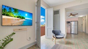 A room with a TV displaying a beach scene, a chair, a door leading to another room, and a kitchen area with appliances. - Fancy Rooftop Retreat in a Central Spot of Miramar (San Juan)