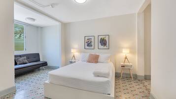 Un dormitorio con una cama grande, un sofá, dos lámparas de noche y una ventana.