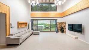 A spacious living room with a sectional sofa, a flat-screen TV mounted on the wall, and a large sliding glass door leading to an outdoor area. - Gangneung Taurus Pension (Gangneung)