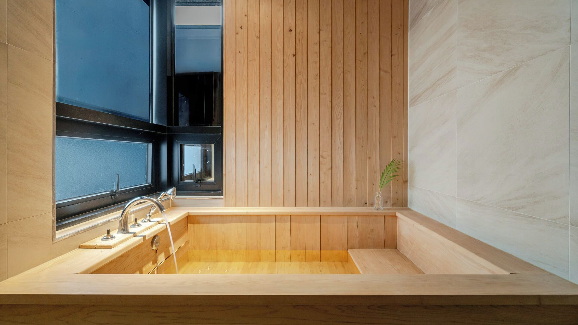 A modern bathroom with a wooden bathtub, a window, and a plant.