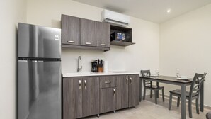 A compact kitchen with a stainless steel refrigerator, dark wooden cabinets, a white countertop, and a dining area with a table and chairs. - Palmbeach 623: 5 min walk to beach  by Bocobay (Noord)