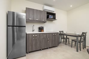 A compact kitchen with a stainless steel refrigerator, dark wooden cabinets, a white countertop, and a dining area with a table and chairs.