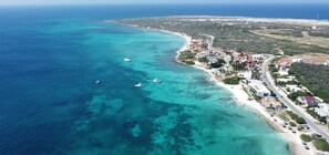 Vista aérea de un pueblo costero con aguas turquesas cristalinas, una playa de arena y una combinación de edificios residenciales y comerciales.