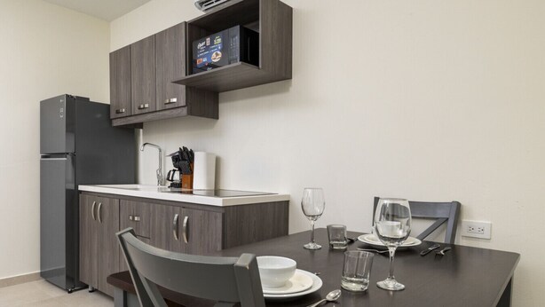 A modern kitchen with dark cabinetry, a built-in oven, and a dining table set for two with wine glasses and plates. - Palmbeach 623: 5 min walk to beach  by Bocobay (Noord)