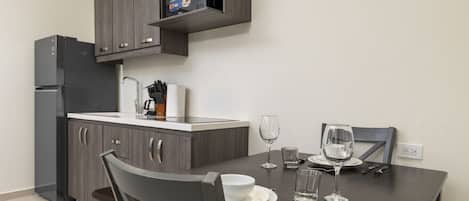 A modern kitchen with dark cabinetry, a built-in oven, and a dining table set for two with wine glasses and plates.