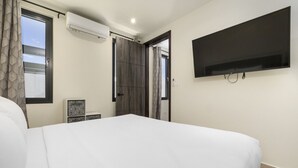 A hotel room with a large bed, a flat-screen TV mounted on the wall, a window with curtains, and an air conditioning unit. - Palmbeach 623: 5 min walk to beach  by Bocobay (Noord)