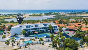 A modern hotel with multiple floors, a swimming pool, and a view of the ocean.