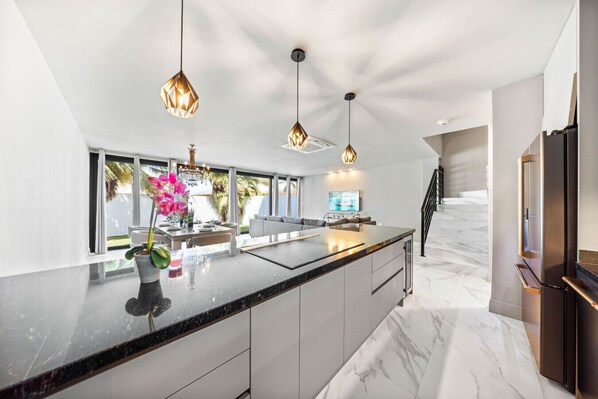A modern kitchen with a large island, pendant lights, and a view to the outdoors.