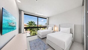 A modern hotel room with a large window, two beds, a desk, and a painting of a sailboat.