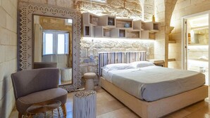 A bedroom with a stone wall, a large bed, a chair, a mirror, and built-in shelves. - Bed & Breakfast in Maglie with 1 bedrooms sleeps 2 (Maglie)