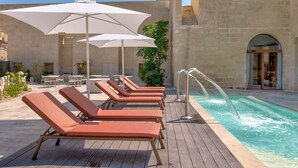 Ein Poolbereich mit Liegestühlen, Sonnenschirmen und einem Wasserspiel.