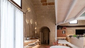 Un interior espacioso con pared de piedra, techo de madera y comedor con sillas rojas y una mesa blanca.