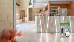 Un vestíbulo amplio con una pared de piedra, un mostrador de recepción y una zona de cocina al fondo.