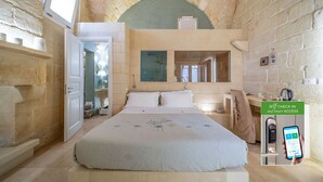 A hotel room with a stone wall, a bed with a floral bedspread, a desk with a chair, and a self-check-in kiosk. - Bed & Breakfast in Maglie with 1 bedrooms sleeps 2 (Maglie)
