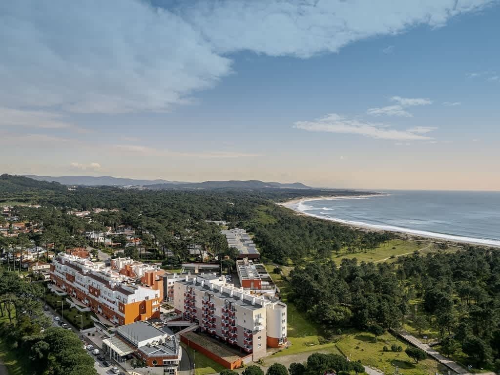 A coastal hotel with multiple buildings, a beach view, and a forested area.
