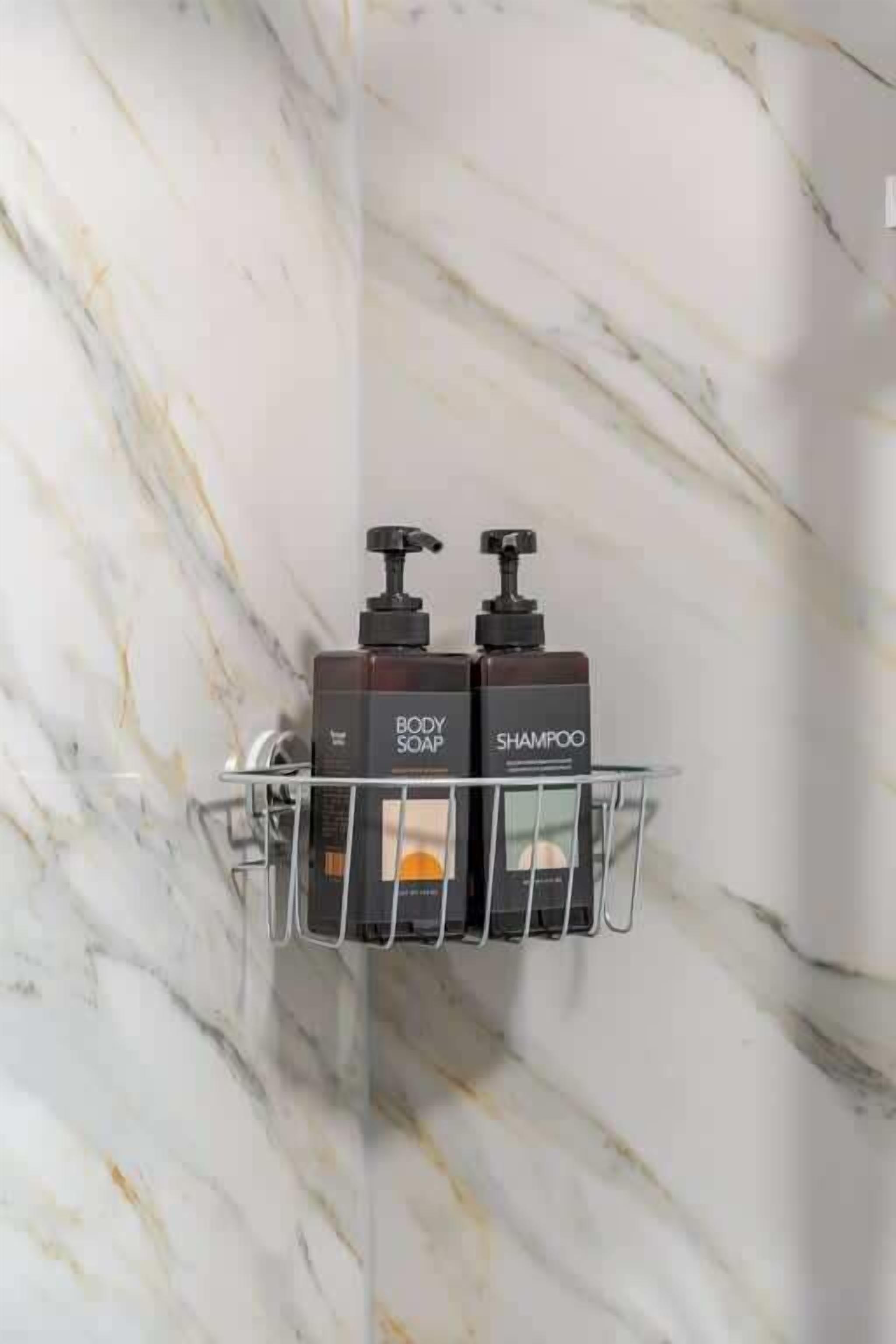 Une salle de bain aux murs recouverts de marbre, avec un présentoir en métal sur lequel sont posés deux flacons de savon liquide et de shampoing.