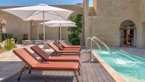 Ein Poolbereich mit Liegestühlen, Sonnenschirmen und einem Wasserspiel.