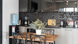 A modern kitchen with black cabinets, a wooden dining table, and a potted plant. - Loocid Apartments at Nova (Nairobi)
