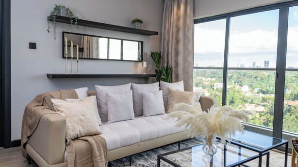 A modern living room with a large window, a sofa, a coffee table, and a mirror. - Loocid Apartments at Nova (Nairobi)