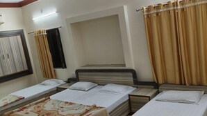 Een hotelkamer met drie bedden, een raam met gordijnen en een wandlamp.