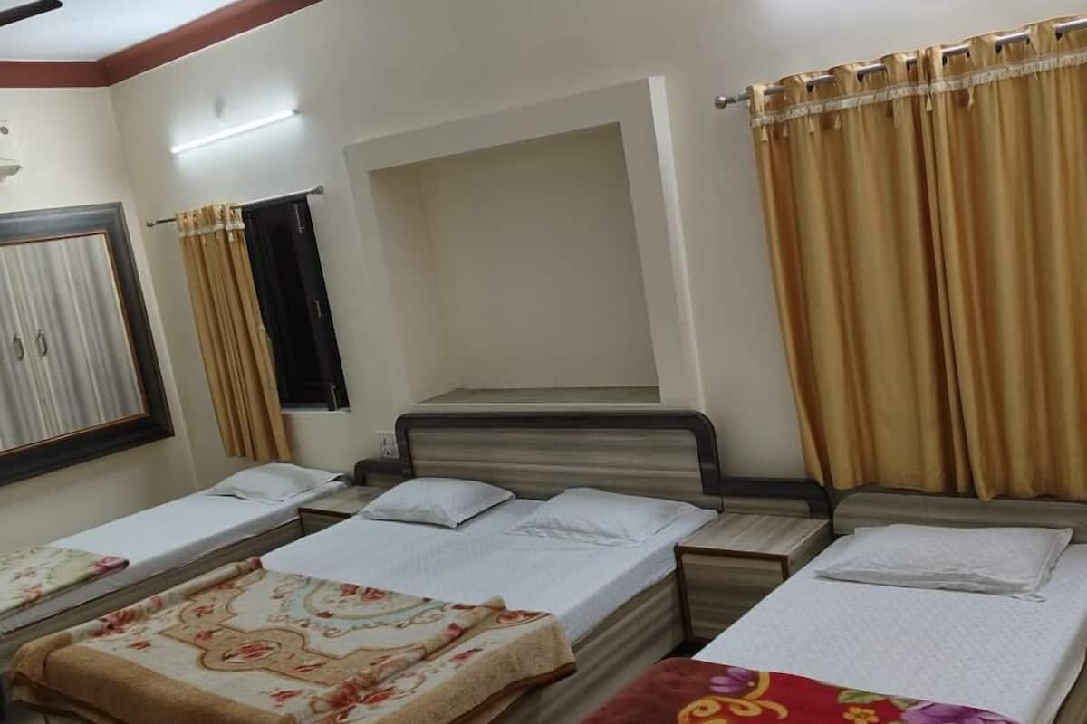 Ein Hotelzimmer mit drei Betten, einem Fenster mit Vorhängen und einer Wandleuchte.