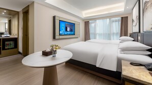 Ein Hotelzimmer mit einem großen Bett, einem runden Tisch, einem an der Wand montierten Fernseher und Blick ins Freie.