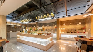 Eine moderne Hotelhalle mit einer zentralen Buffettheke, Sitzgelegenheiten und einer im Hintergrund sichtbaren Küche.